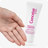 For Conceive Plus Fertility Lubricant Tube + Applicators (PT), a 75ml fertility lubricant tube beside a human hand displaying a small amount of clear gel on palm, visually demonstrating texture and consistency of fertility-safe lubricant for customers seeking ease and realism.
