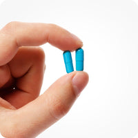 A hand holding two blue Conceive Plus Men's Fertility Support capsules. Image highlights the compact vegan capsule form of the male fertility supplement.